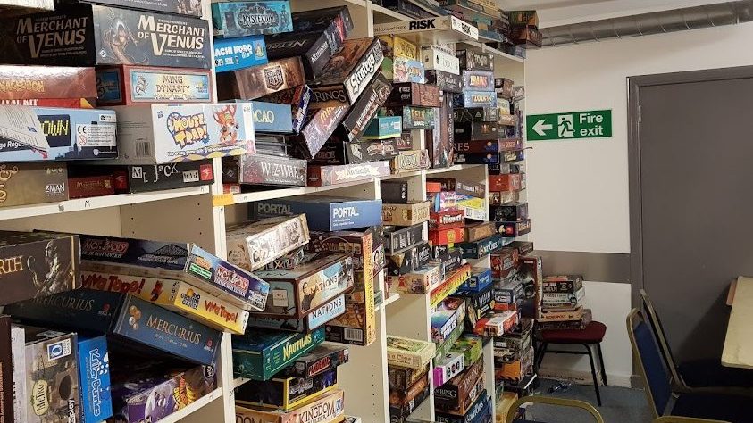Shelves at Games Hub stacked floor-to-ceiling with board games — Risk, Portal, Wiz-War, Merchant of Venus and hundreds more