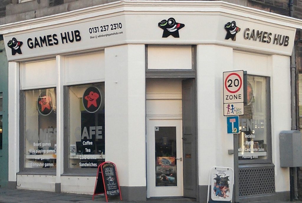 The white corner shopfront of Games Hub on Lauriston Place, Edinburgh, with the grinning black meeple above the door